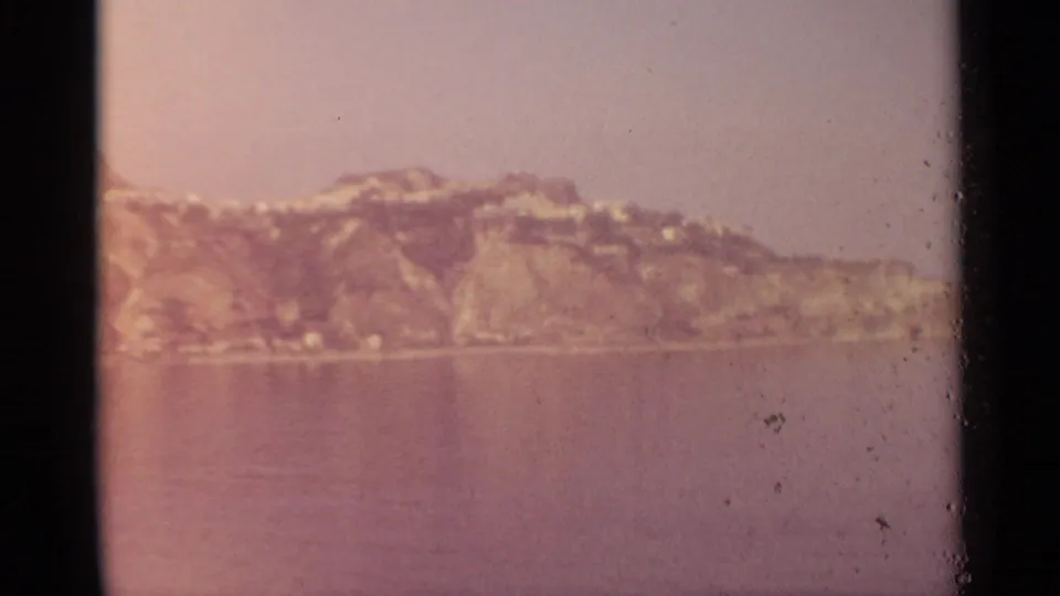 The cliffside and water remain visible, with stronger pink fading, dust marks, and the soft texture of aged 8mm film.