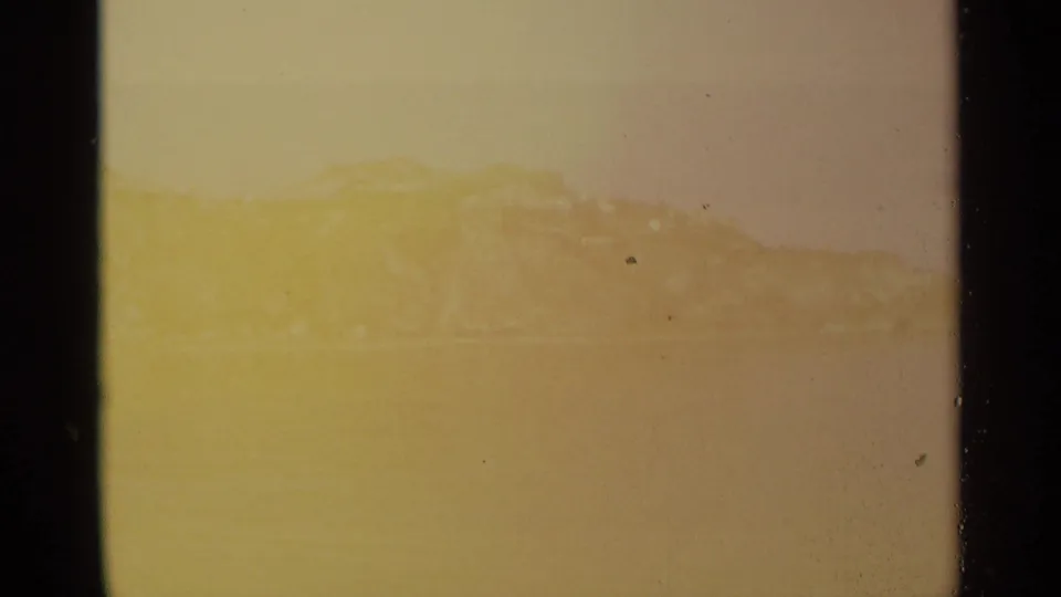 The final frame is strongly yellowed and scratched, leaving only a faint view of the distant cliff and water through the film damage.