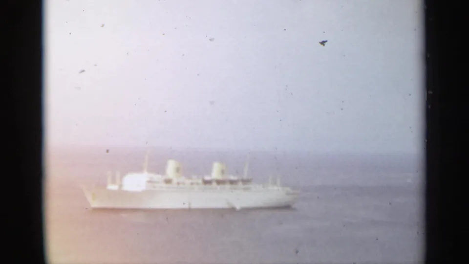 Distant white ship on the water in the Stockholm 1965 reel, seen through soft exposure and visible 8mm film grain.