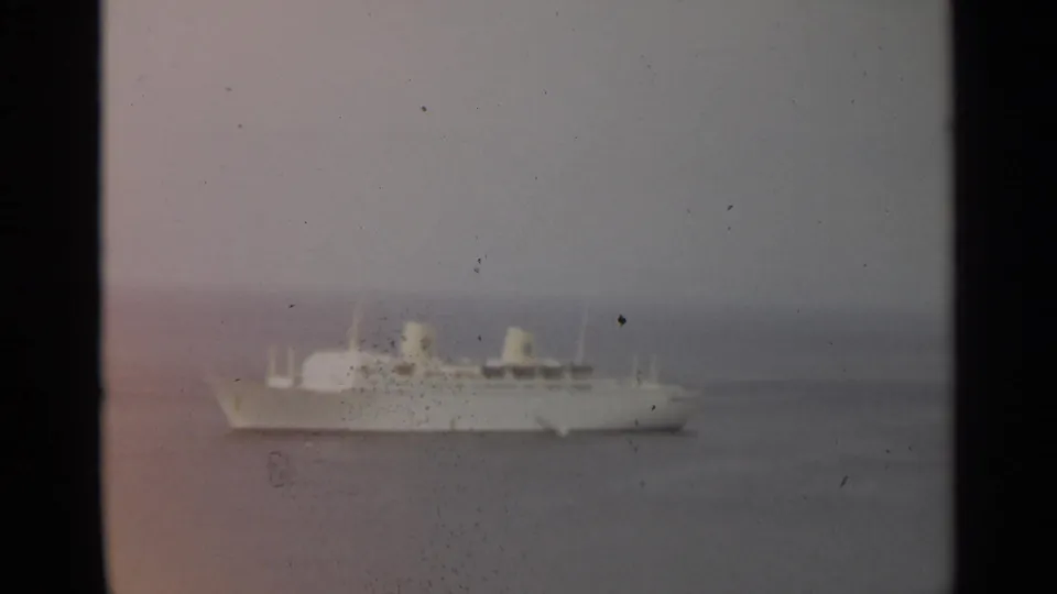 Distant white passenger ship in a soft 8mm frame, with twin funnels visible against cloudy water and sky near Stockholm.