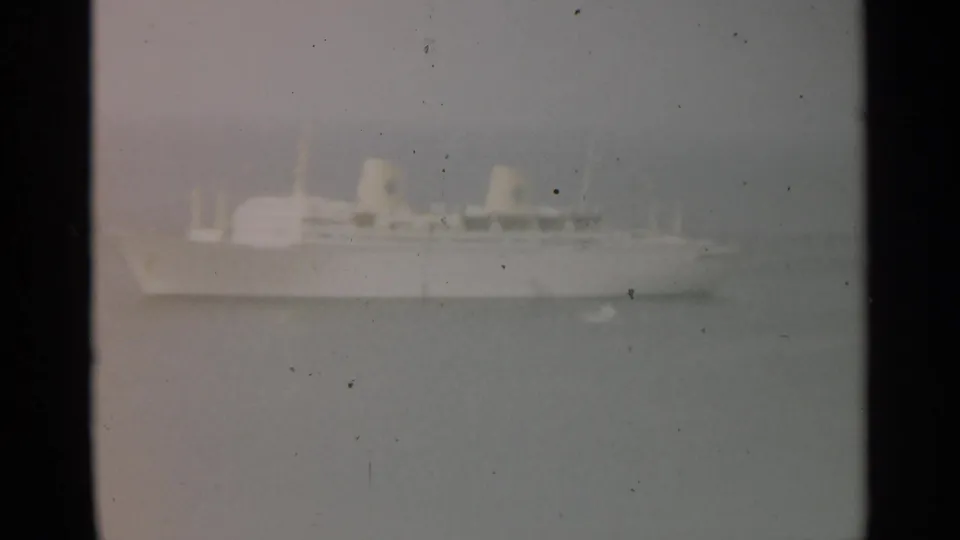 Closer 8mm view of the white passenger ship, with deck forms and funnels softened by haze and film grain.