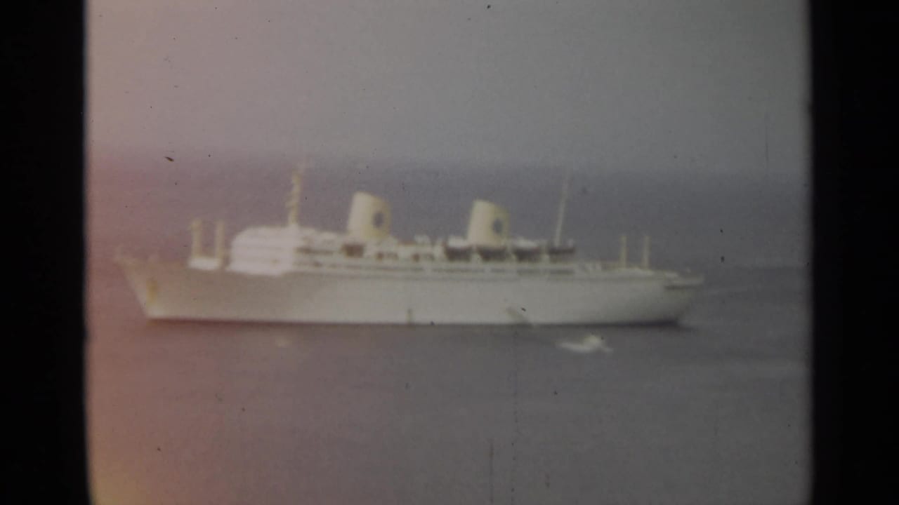 Large white passenger ship on hazy water with twin funnels visible.