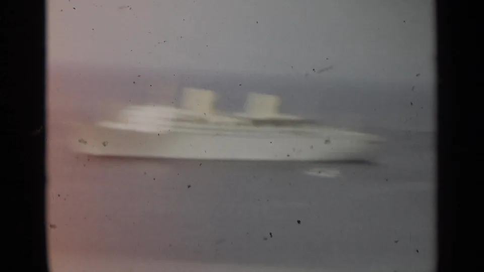 Soft 1965 Stockholm 8mm frame of a white passenger ship seen from a distance across gray-blue water.