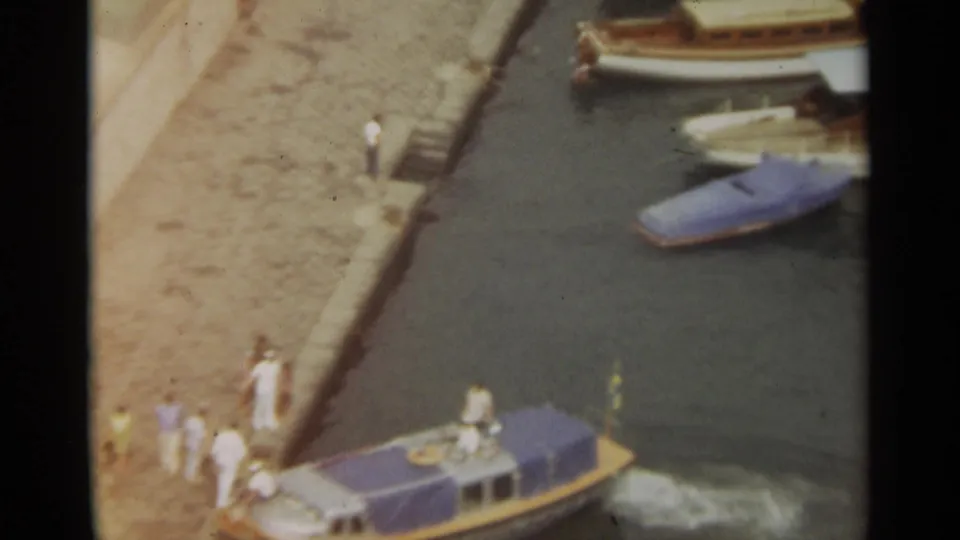 Stockholm harbor frame from 1965 showing a small motorboat with a blue canopy at a stone quay as people stand nearby.