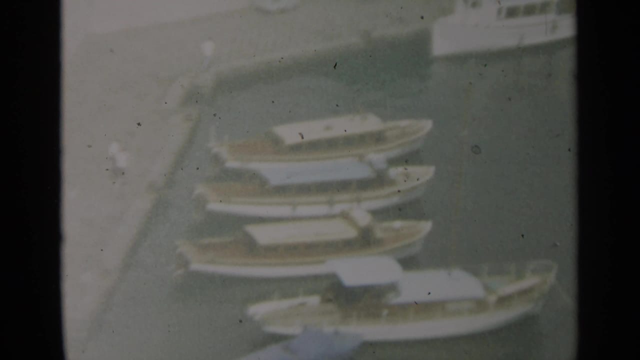 Elevated 1965 Stockholm harbor view of several small boats moored close together on dark water.