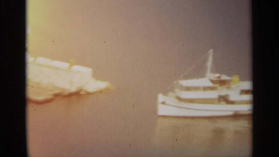 1965 Stockholm harbor frame showing a passenger boat beside a pale stone pier, with warm color fading and dark film edges.