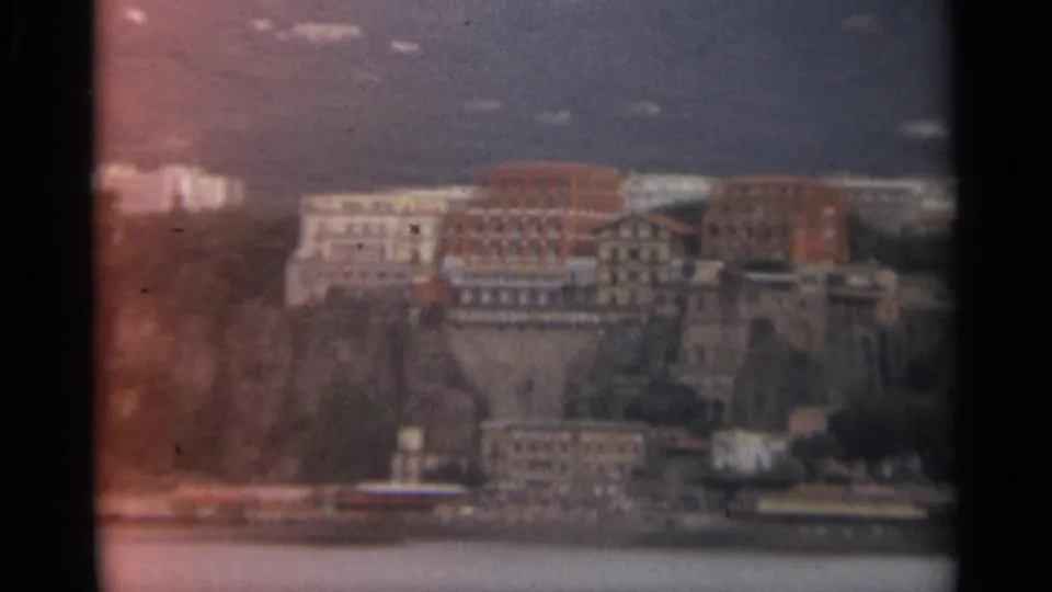 1965 Stockholm waterfront view with hillside buildings, shoreline structures, water, and soft home-movie grain.