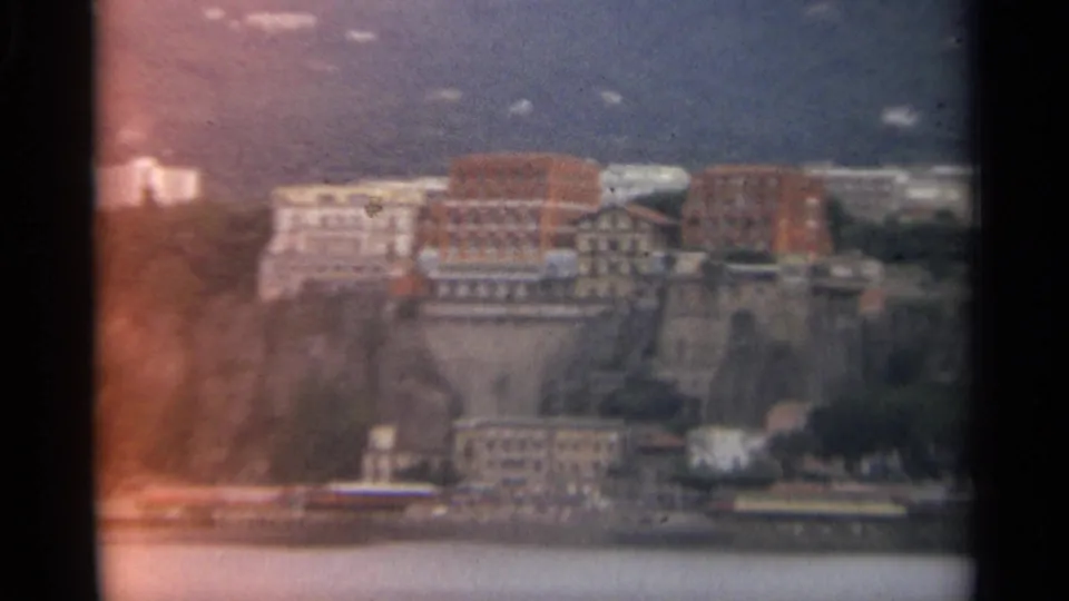 1965 Stockholm hillside waterfront with dense buildings over the water, softened by faded color and visible 8mm film texture.