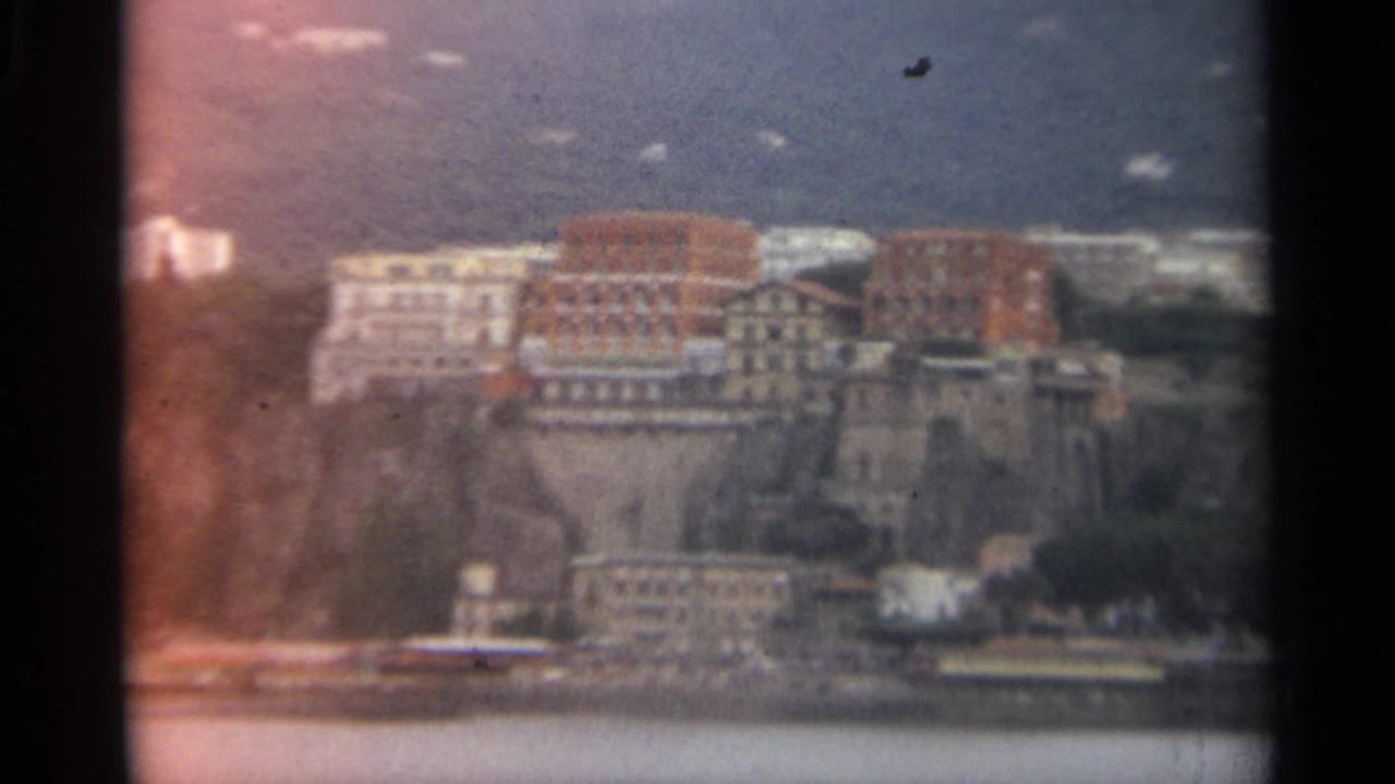 Distant cliffside buildings above a broad body of water, framed by dark film edges.