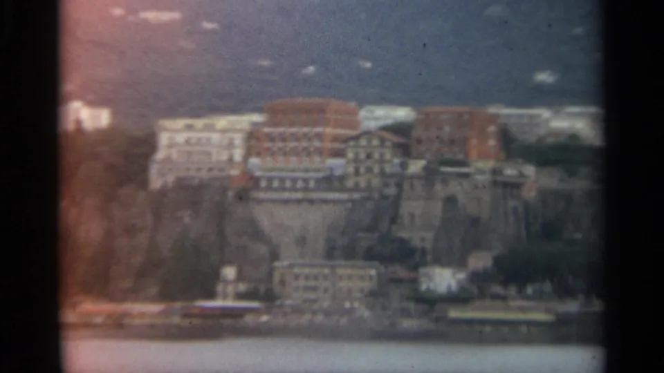 Stockholm waterfront buildings sit above a rocky cliff in a soft, grainy 1965 home-movie frame.