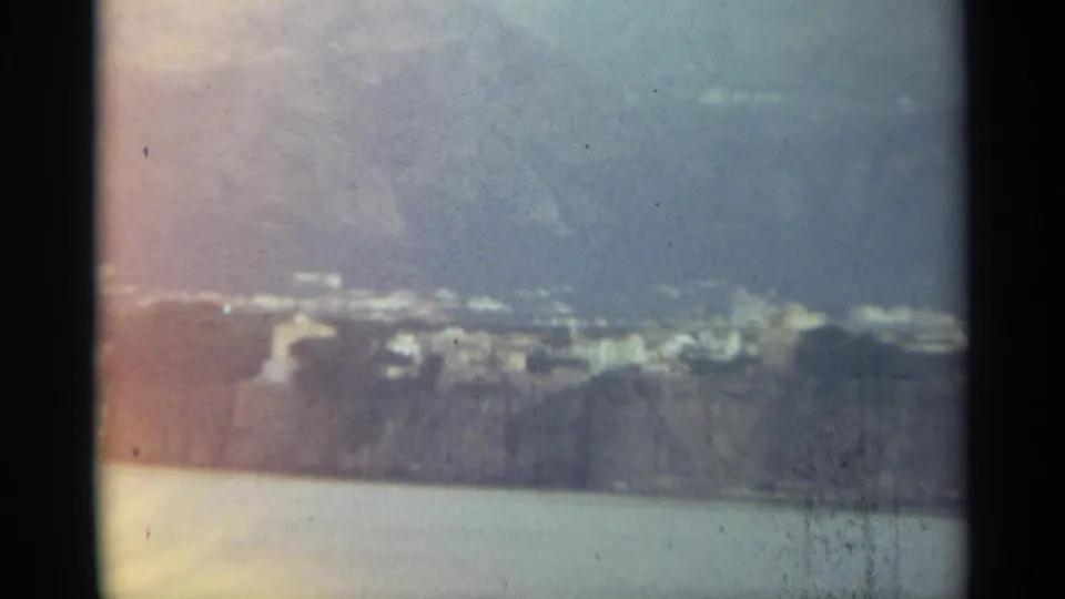Soft 8mm frame from Stockholm in 1965, showing distant shoreline buildings and rocky land beyond the water.