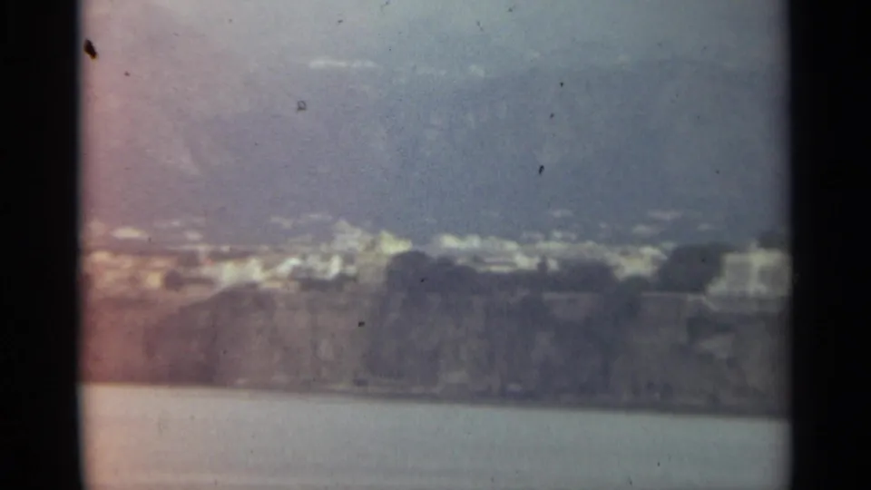 End frame of a 1965 Stockholm waterfront view, with distant buildings and rocky cliff forms softened by 8mm film texture.