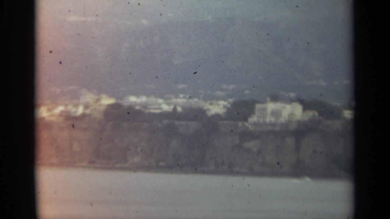 Distant white buildings on a rocky shoreline above calm water.