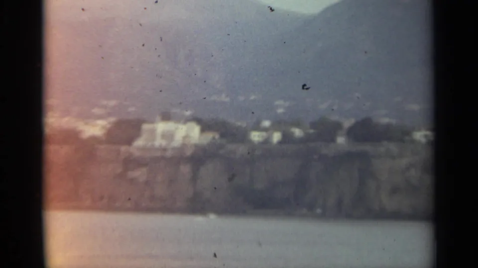 Soft 8mm view of a Stockholm waterfront hillside with pale buildings, rocky cliffs, and water in the foreground.