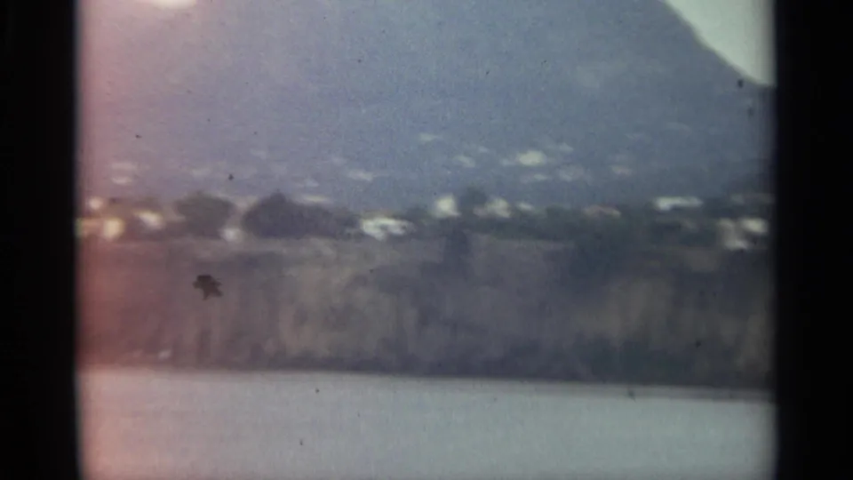 1965 Stockholm travel frame showing scattered buildings on a green hillside above a rocky waterfront.
