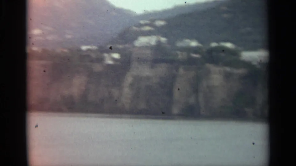 A soft 8mm frame of Stockholm waterfront cliffs with hillside buildings, water, and muted overcast light.