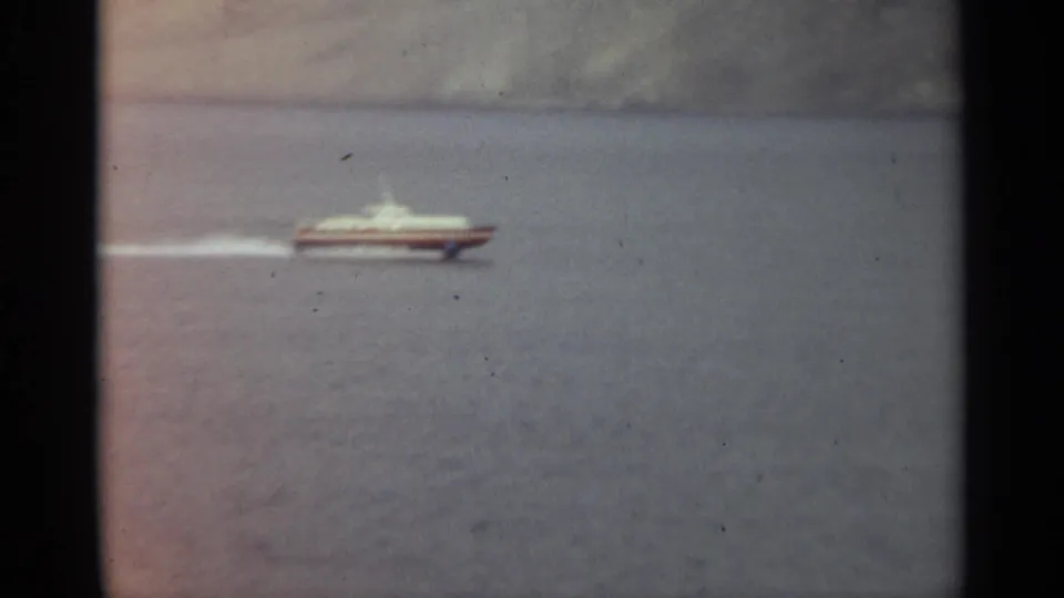 A distant white-and-red hydrofoil continues across Stockholm water, framed by faded 8mm color and grain.