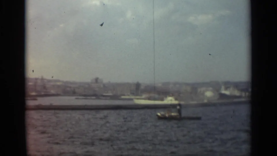 Stockholm harbor in 1965, showing a small motorboat in the foreground water and a larger white vessel near the distant waterfront.