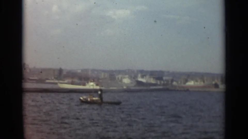 1965 Stockholm harbor view with a small tugboat in the foreground and larger vessels along a hazy waterfront.