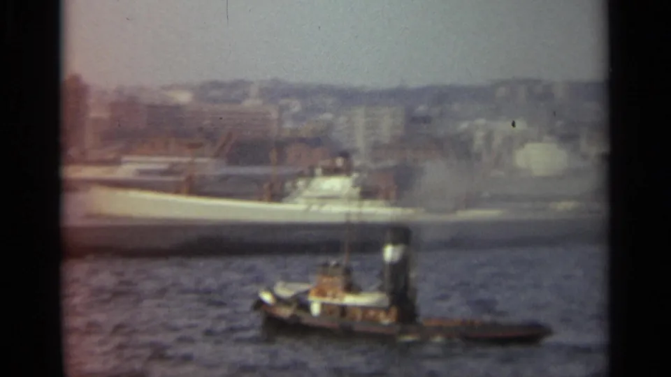 Closer 1965 Stockholm harbor frame with tugboat, dock structure, and a large white ship behind the foreground water.