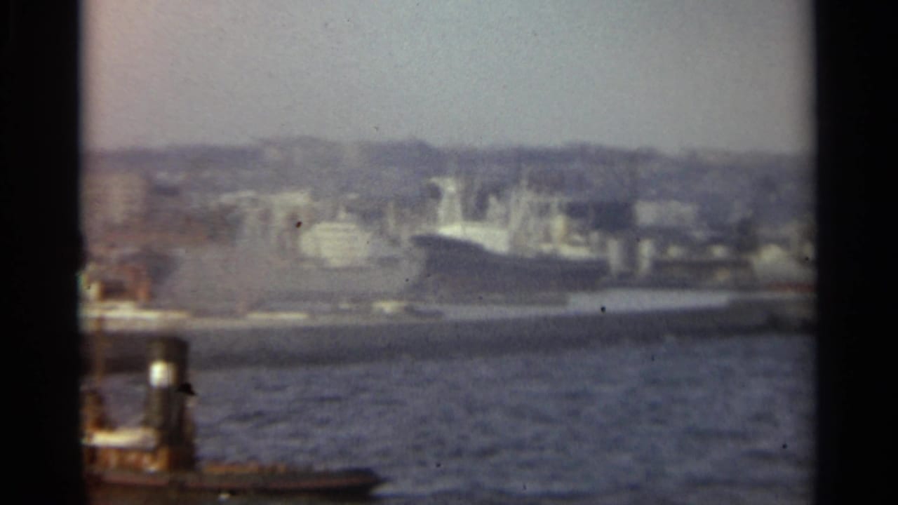 1965 Stockholm harbor view with rippled water, docked vessels, waterfront buildings, and distant hills in soft color 8mm.