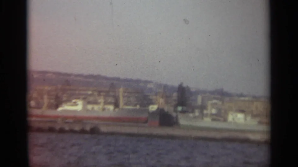 End of the 1965 Stockholm harbor pan, showing a docked vessel, city waterfront, rippled water, and visible 8mm frame edge.