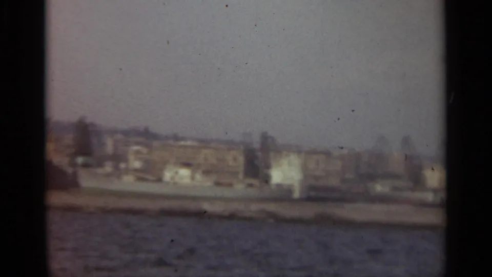 1965 Stockholm harbor shoreline with old buildings, dark tree shapes, and water in the foreground.