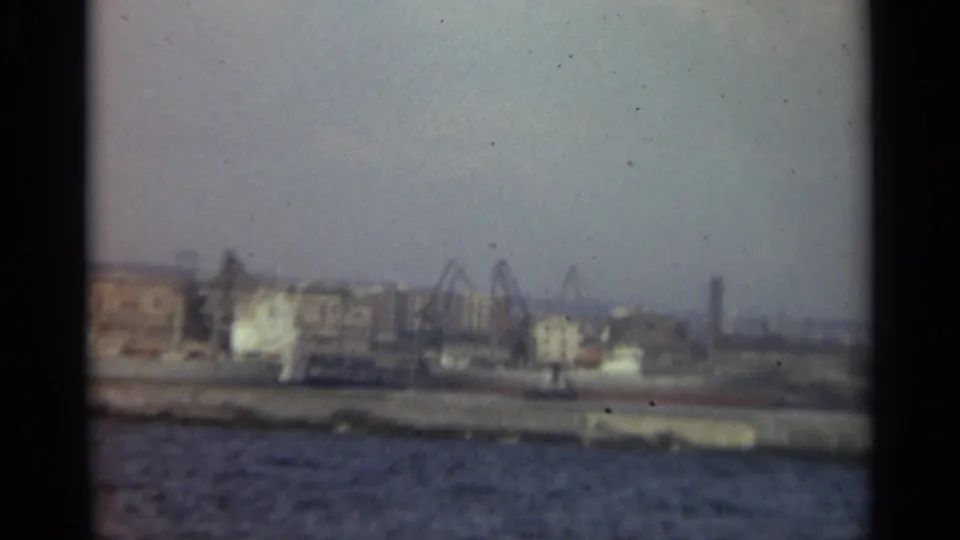 1965 Stockholm industrial waterfront showing cranes, dock structures, low buildings, and rippled harbor water.