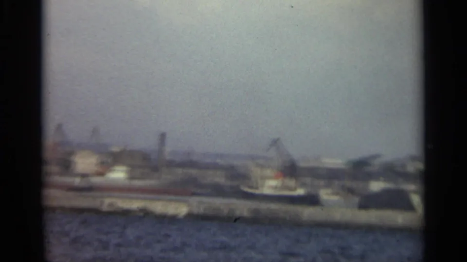 1965 Stockholm waterfront with a long quay, cranes, dockside buildings, and water under a hazy sky.