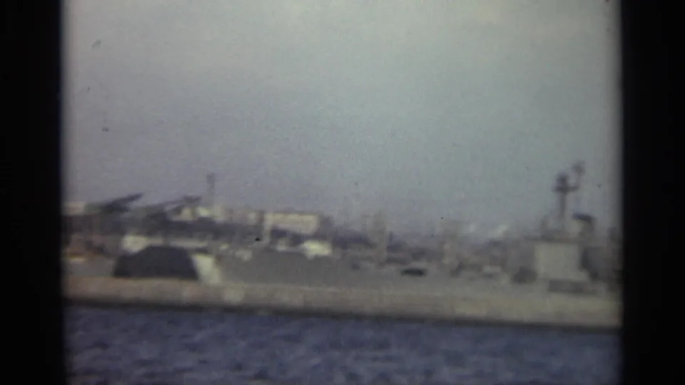 1965 Stockholm waterfront view with dark harbor water, low industrial buildings, cranes, and a small structure near the shore.