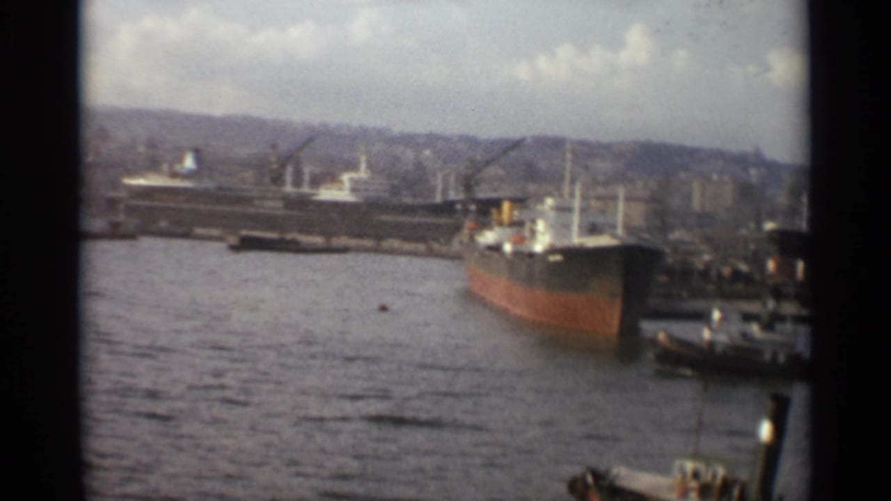 A red-hulled freighter near the quay with harbor cranes and small boats nearby.