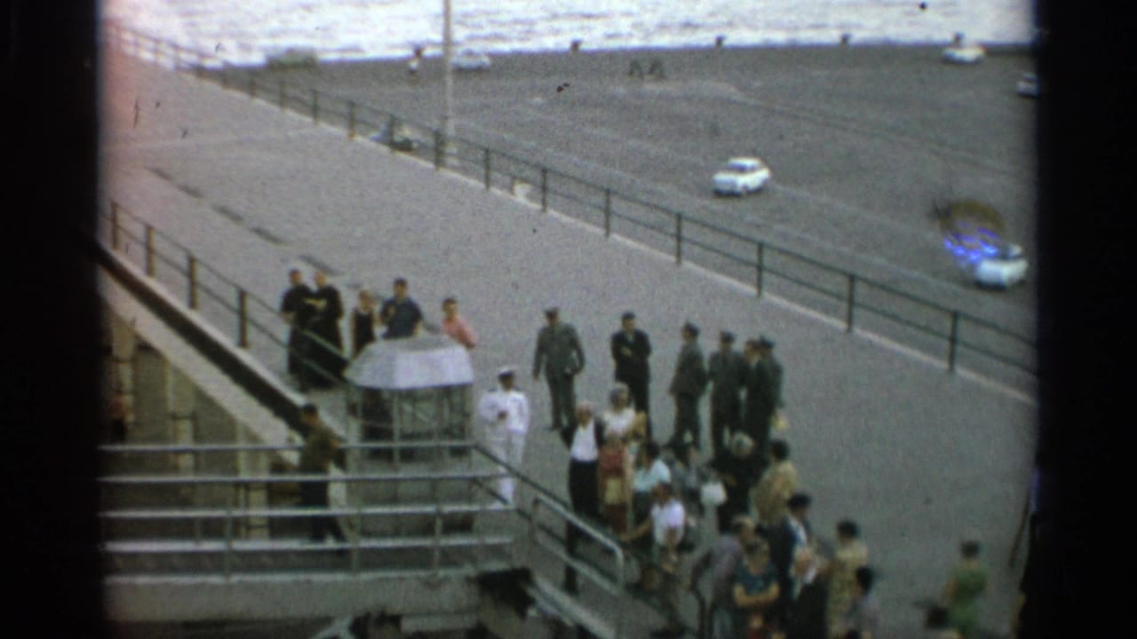 Stockholm pier scene from 1965 with a gathered crowd, several uniformed figures, railings, roadway, and parked or passing cars.