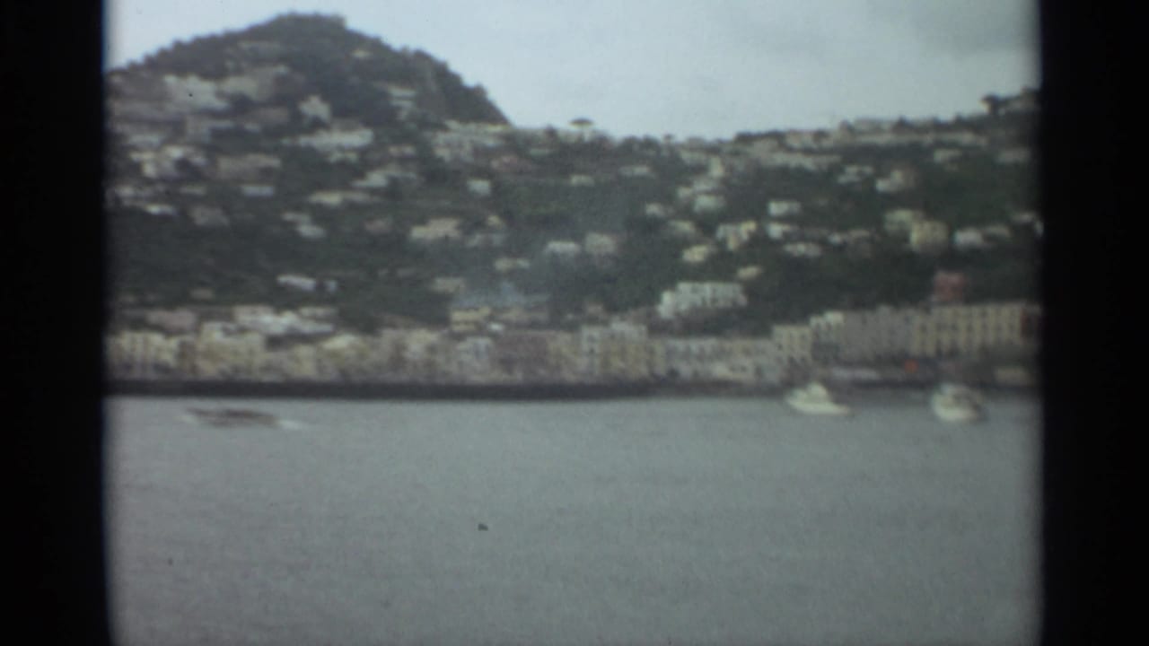 1965 Stockholm waterfront scene with white boats on calm water and hillside houses rising behind shorefront buildings.