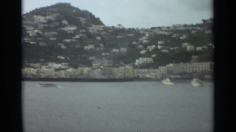 1965 Stockholm waterfront scene with white boats on calm water and hillside houses rising behind shorefront buildings.