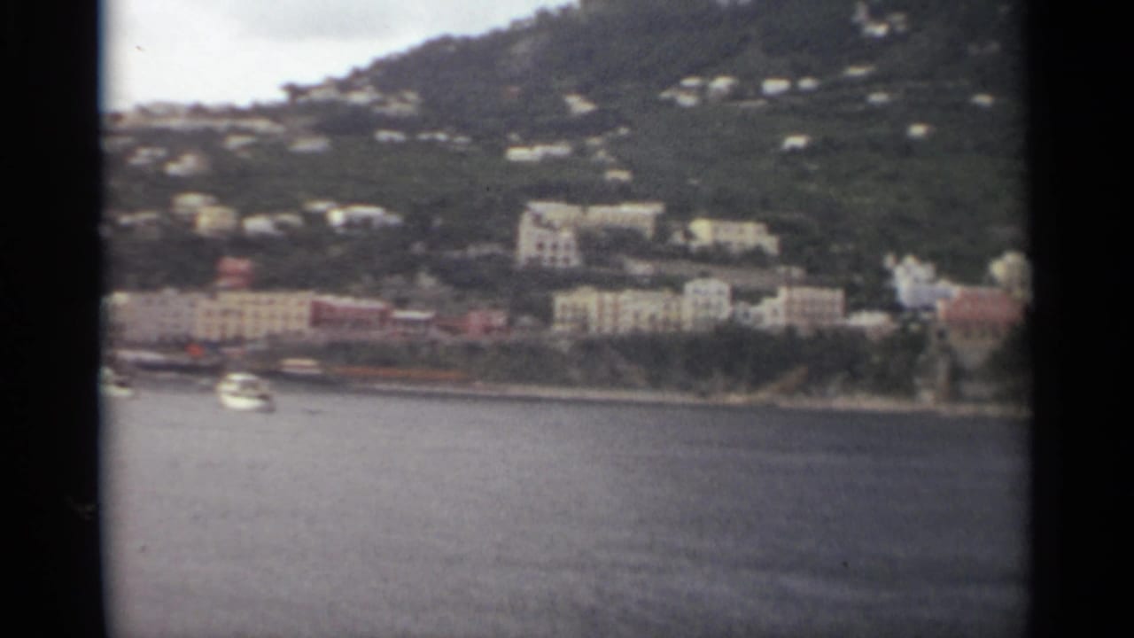 Soft 8mm frame of a Stockholm shoreline with one visible boat, clustered buildings, and homes scattered across the green slope.
