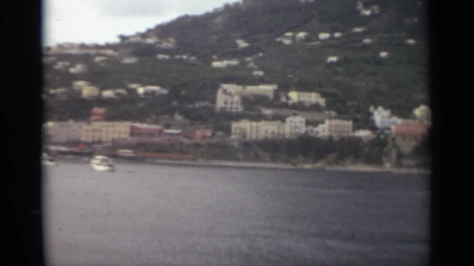 Soft 8mm frame of a Stockholm shoreline with one visible boat, clustered buildings, and homes scattered across the green slope.