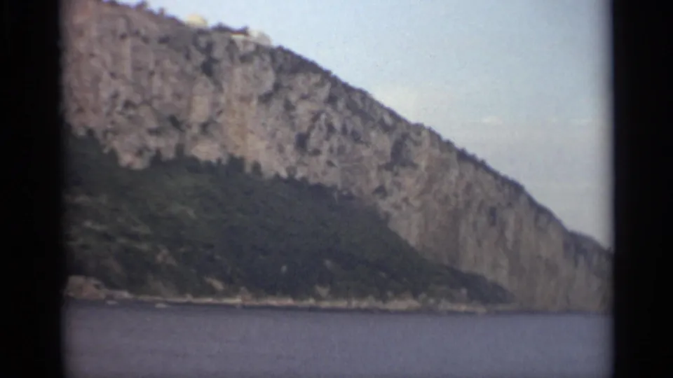 1965 Stockholm coastal landscape with a wooded rocky headland, still water, and soft 8mm color and grain.