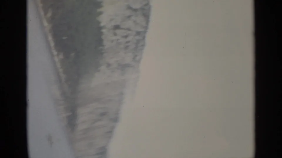 Blurred 1965 8mm Stockholm frame with the shoreline and cliff edge tilted during a handheld camera move over pale water.