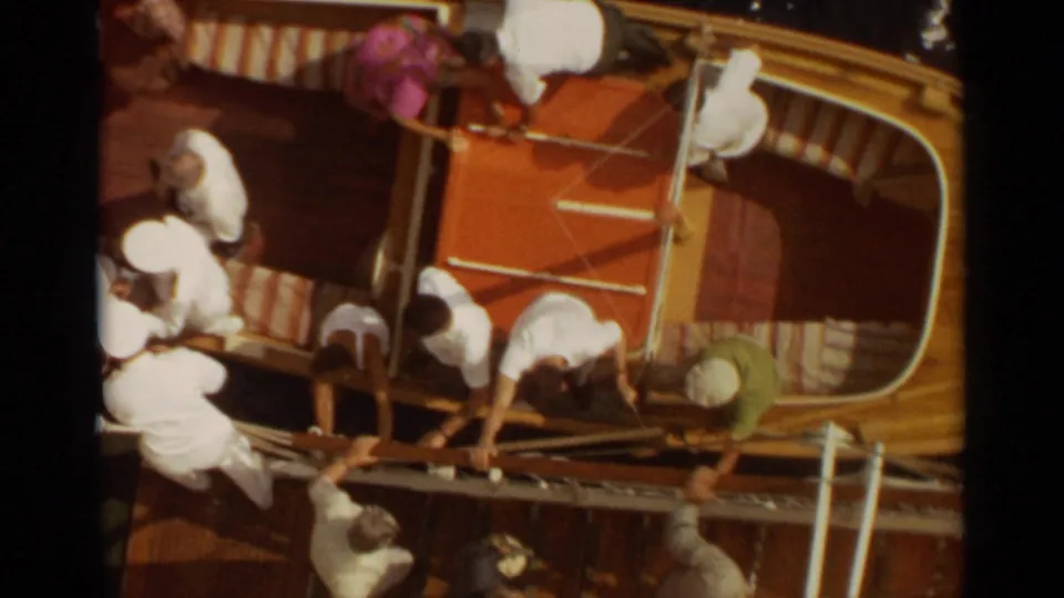 Overhead 1965 home-movie view of several people on a wooden boat deck, with railings and deck fittings visible.