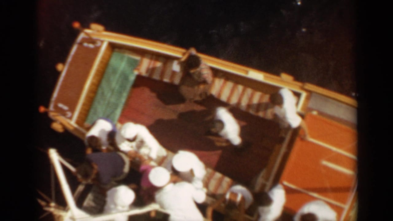 1965 Stockholm frame with passengers gathered at the side of a yellow boat, viewed from above in strong sunlight.
