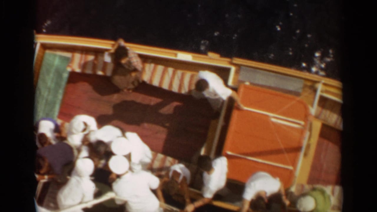 Final 1965 Stockholm 8mm frame showing passengers aboard the yellow boat, with striped seating and dark water around it.