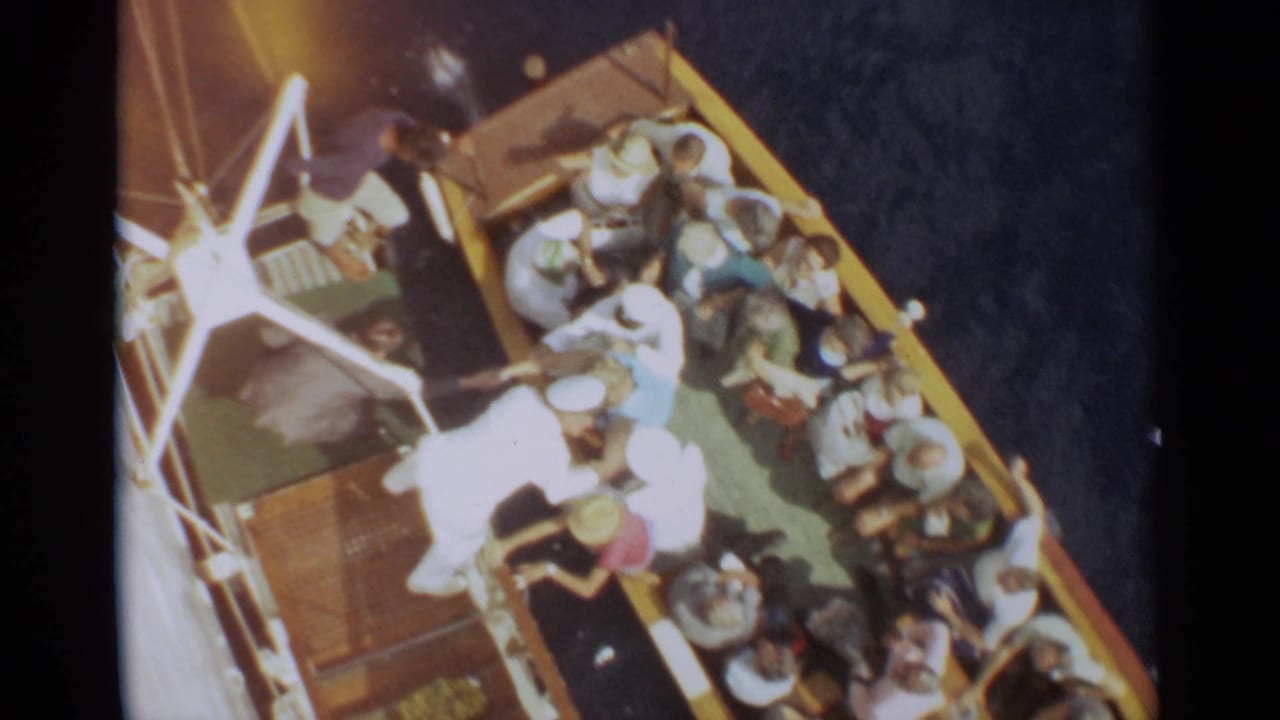 1965 Stockholm home-movie frame showing passengers gathered on a crowded ship deck from an elevated angle.