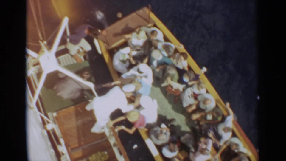 1965 Stockholm home-movie frame showing passengers gathered on a crowded ship deck from an elevated angle.