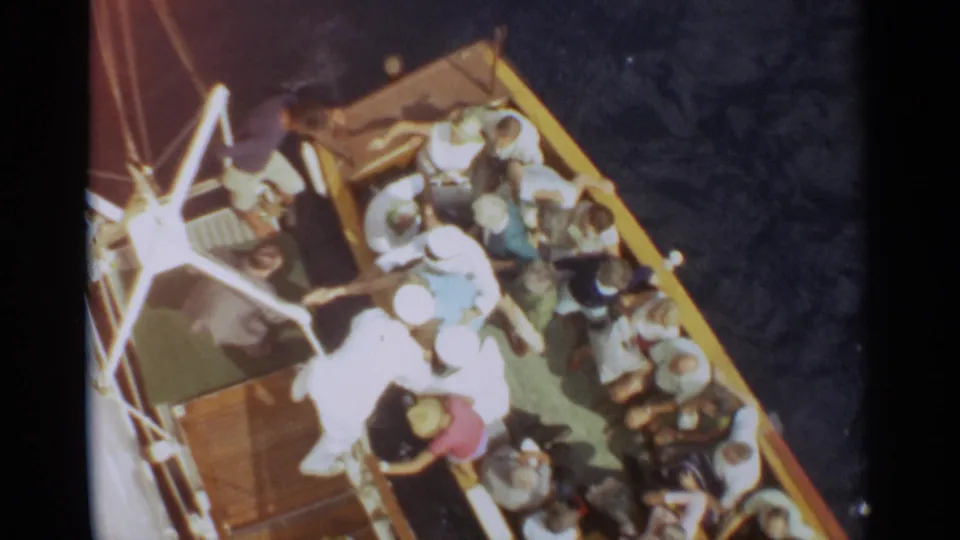 Elevated 8mm view of a crowded Stockholm ship deck with seated and standing passengers in summer clothing.