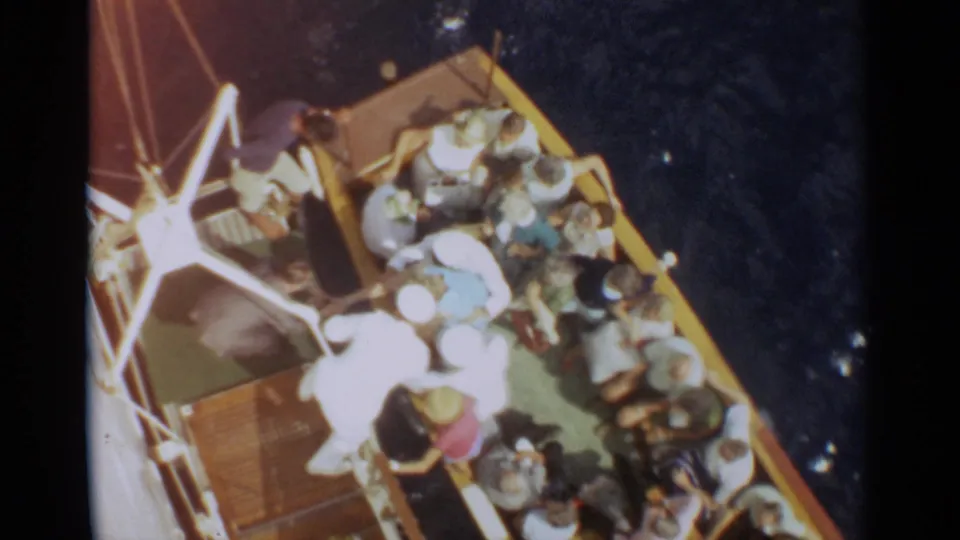 Home-movie frame from Stockholm, 1965, showing adults packed along a ship deck as water passes below.