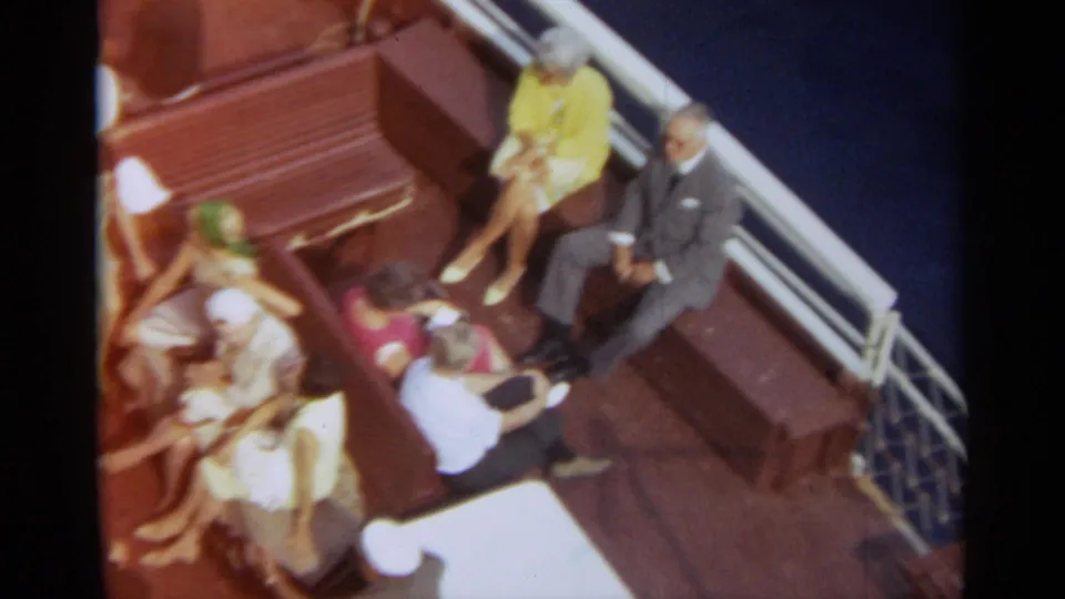 Passengers aboard a Stockholm boat sit near the railings in 1965 footage, with blue water beyond the deck.