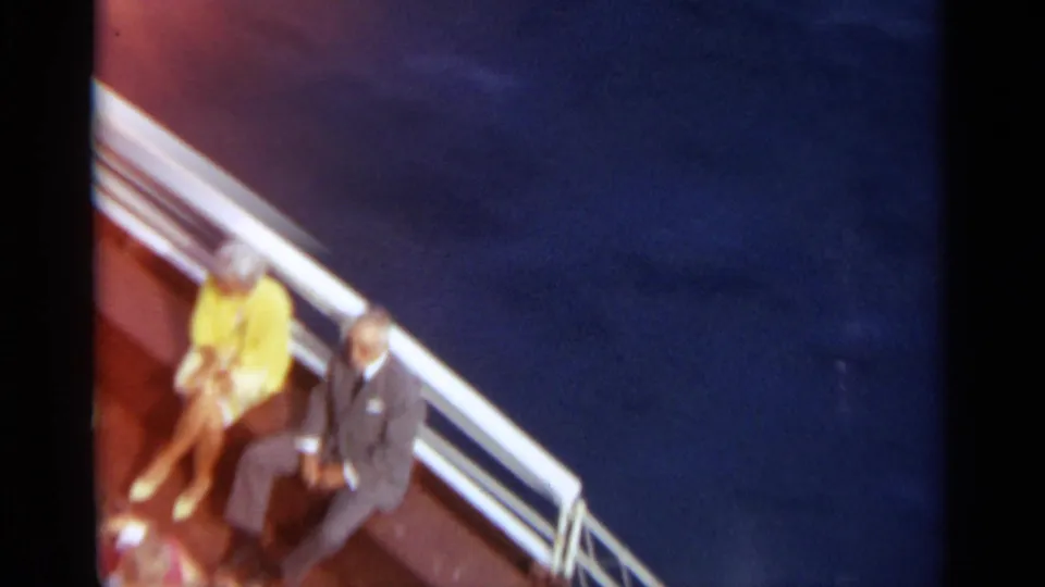 A closer 1965 Stockholm boat-deck frame shows seated passengers near white railings and open blue water.