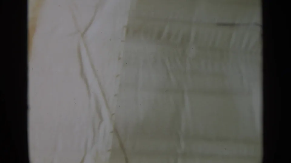 1965 8mm close view of a pale ship deck or canvas-like surface, with faint seams and subdued color fading.