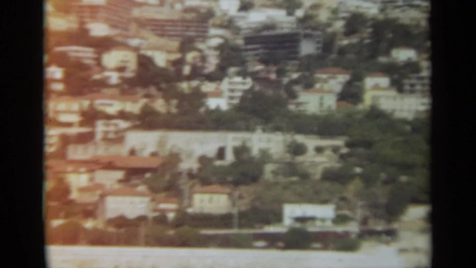 Faded 8mm view of Stockholm with hillside buildings, greenery, and a waterfront edge in soft focus.