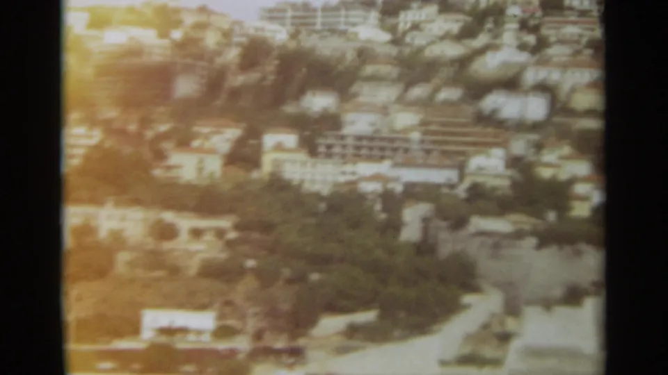1965 Stockholm city view in 8mm color, showing clustered buildings, tree cover, and a road near the water.